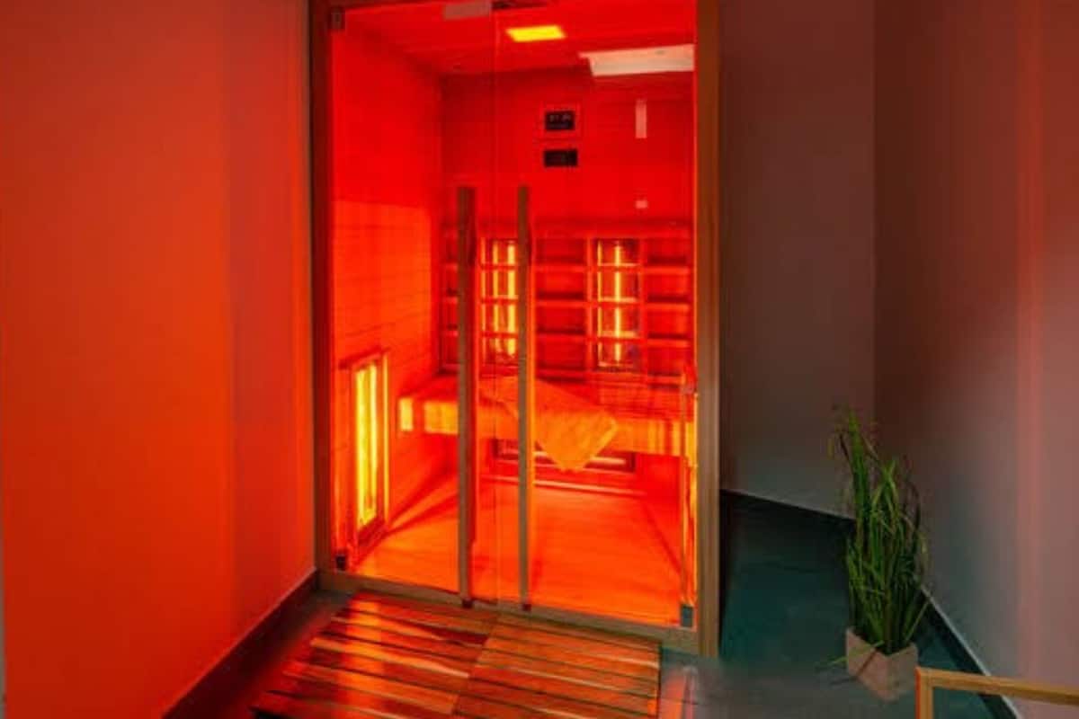 A hallway with a red-lit room at the end, wooden flooring, and a potted plant.