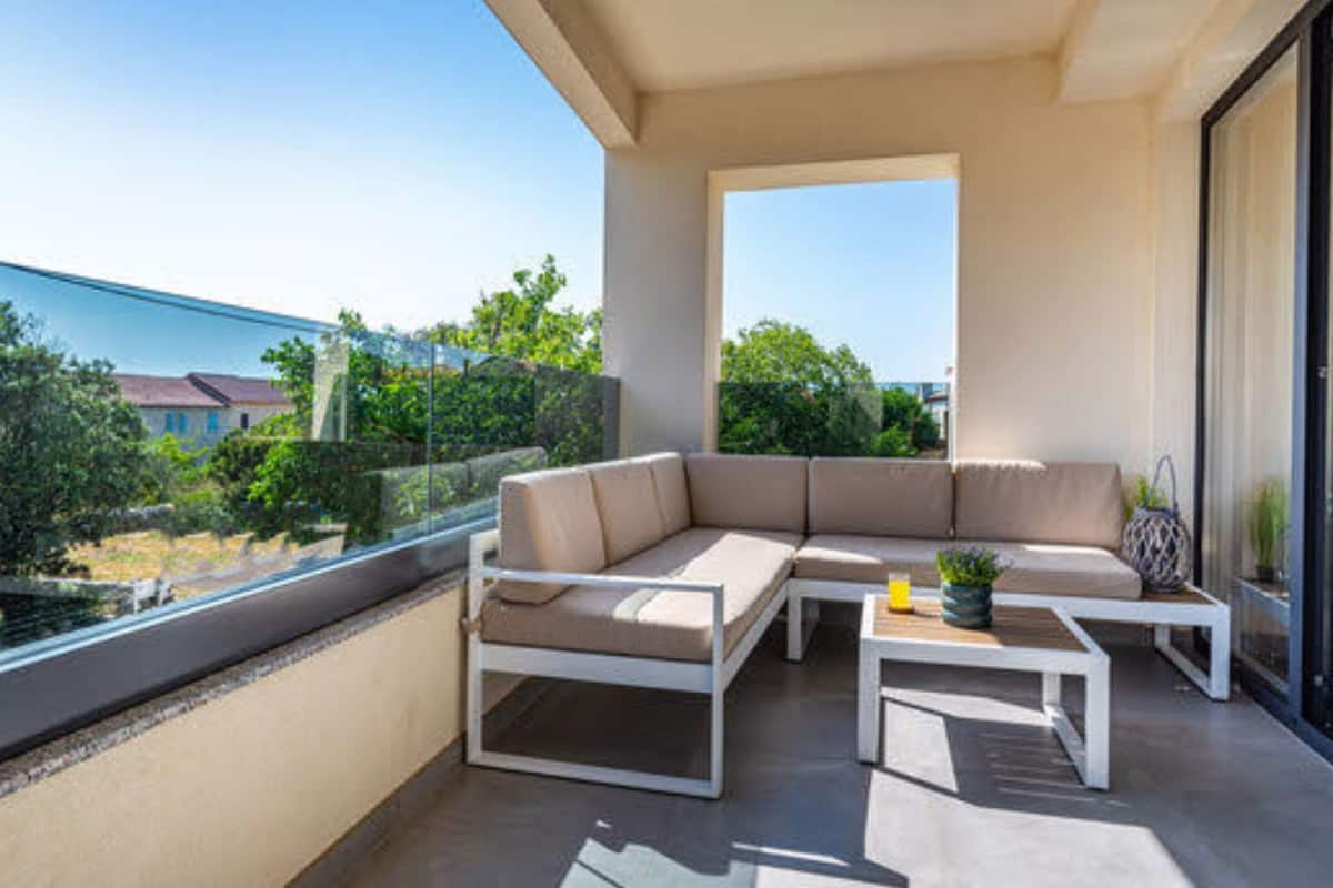 A balcony with a beige sectional sofa, a small table, and a potted plant.