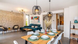 Una sala de estar moderna con pared de piedra, un sofá verde y una zona de comedor con mesa de madera dispuesta para cuatro.