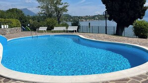 A swimming pool with stone tiles, two white benches, and a view of a lake and mountains. - Stupenda Vista Lago, Appartamento con Piscina (Solarolo)