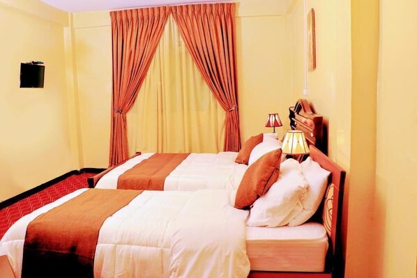 A hotel room with two beds, a red and white striped bedspread, a red and white lamp, and a curtain.