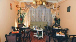 A dining area with a red patterned floor, black upholstered chairs, a white cart with bottles, and a sofa in the background. - Keba Guesthouse (Addis Ababa)