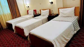 Habitación de hotel con dos camas individuales, una alfombra roja y un ventanal con cortinas.