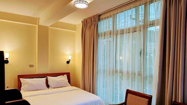 Habitación de hotel con una cama grande, dos lámparas de noche, una silla y un ventanal con cortinas.