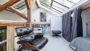 A modern loft bedroom with a skylight, a leather chair, a desk, and a bed.