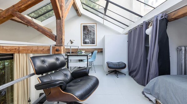 Un dormitorio tipo loft moderno con tragaluces, un sillón de cuero, un escritorio y una cama.