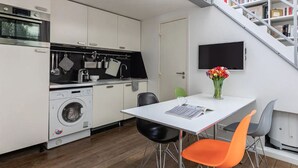A compact kitchen with a washing machine, a dining table with chairs, and a TV mounted on the wall.