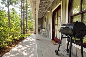 A covered porch with a grill, outdoor seating, and a view of a forested area.