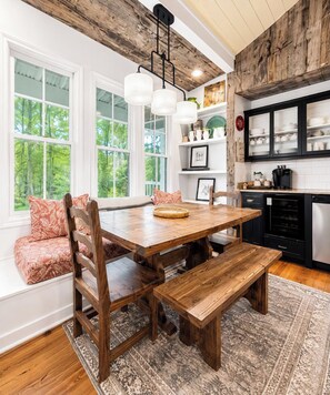A dining area with a wooden table and benches, large windows, and a kitchen with black cabinets.