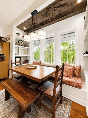 A dining area with a wooden table, benches, and a built-in bench seating area with patterned cushions.