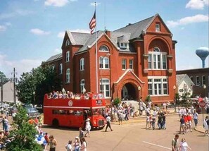 A red double-decker bus in front of a large brick building with arched windows and a flagpole. - The Nest Egg, 3BR Home by Velvet Ditch Villas (Oxford)
