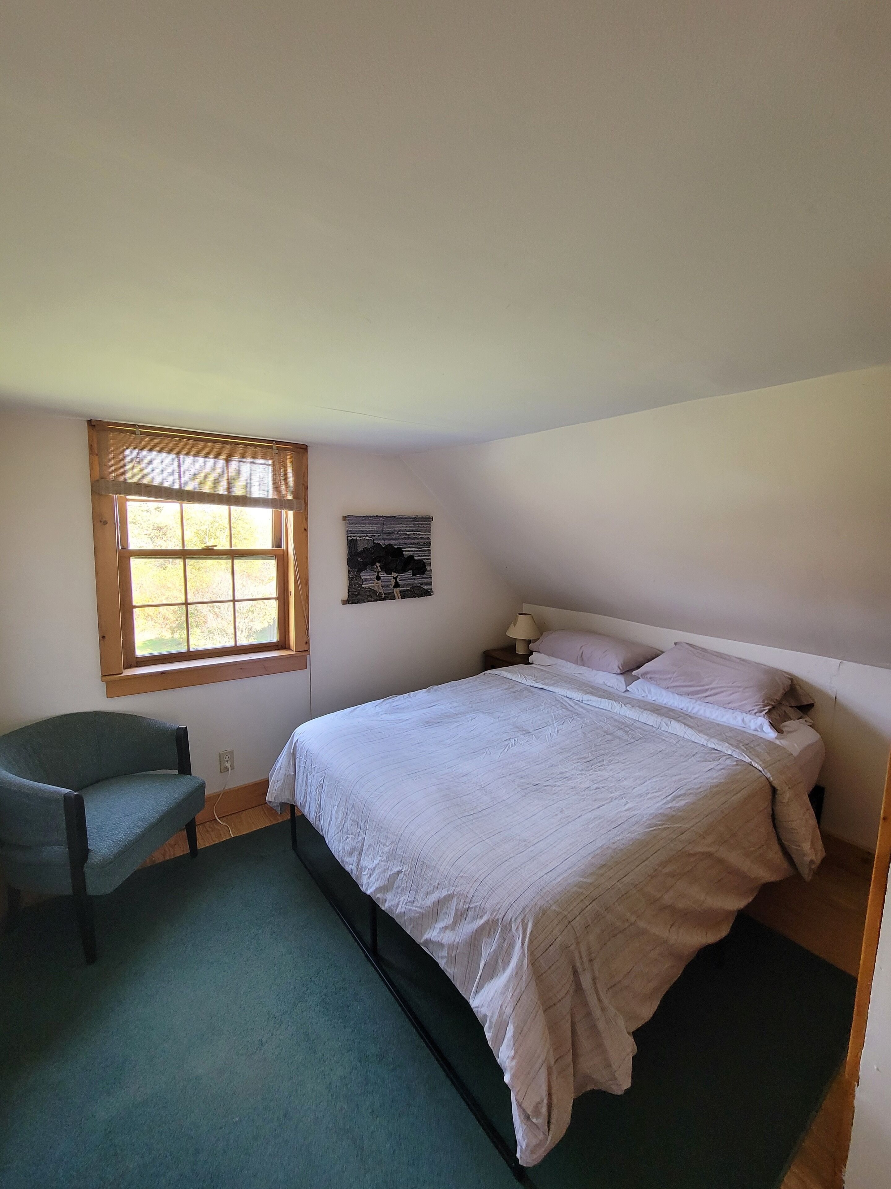 Een slaapkamer met een bed, een stoel, een raam en een aan de muur bevestigd schilderij.