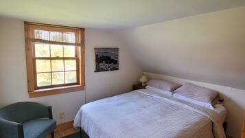 Een slaapkamer met een bed, een stoel, een raam en een aan de muur bevestigd schilderij.