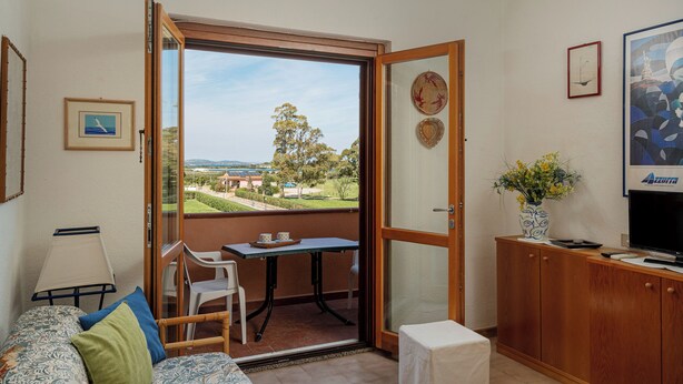 A room with a balcony, a dining table, a TV, and a cabinet. - Casa Rosella by Wonderful Italy (Olbia)