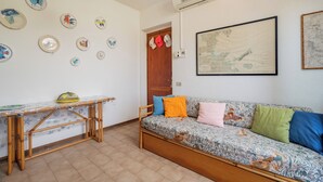 A room with a wooden table, a sofa with colorful cushions, and wall-mounted decorative plates. - Casa Rosella by Wonderful Italy (Olbia)