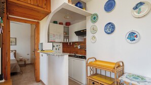 A compact kitchen with white cabinets, a wooden countertop, and a wicker side table. - Casa Rosella by Wonderful Italy (Olbia)