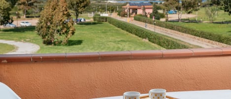 Un balcón con una mesa dispuesta para dos personas, con vista a un jardín ajardinado y edificios a la distancia.