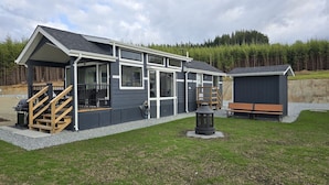 Et moderne hus med en overdækket veranda, en trætrap og et lille udendørs siddeområde.
