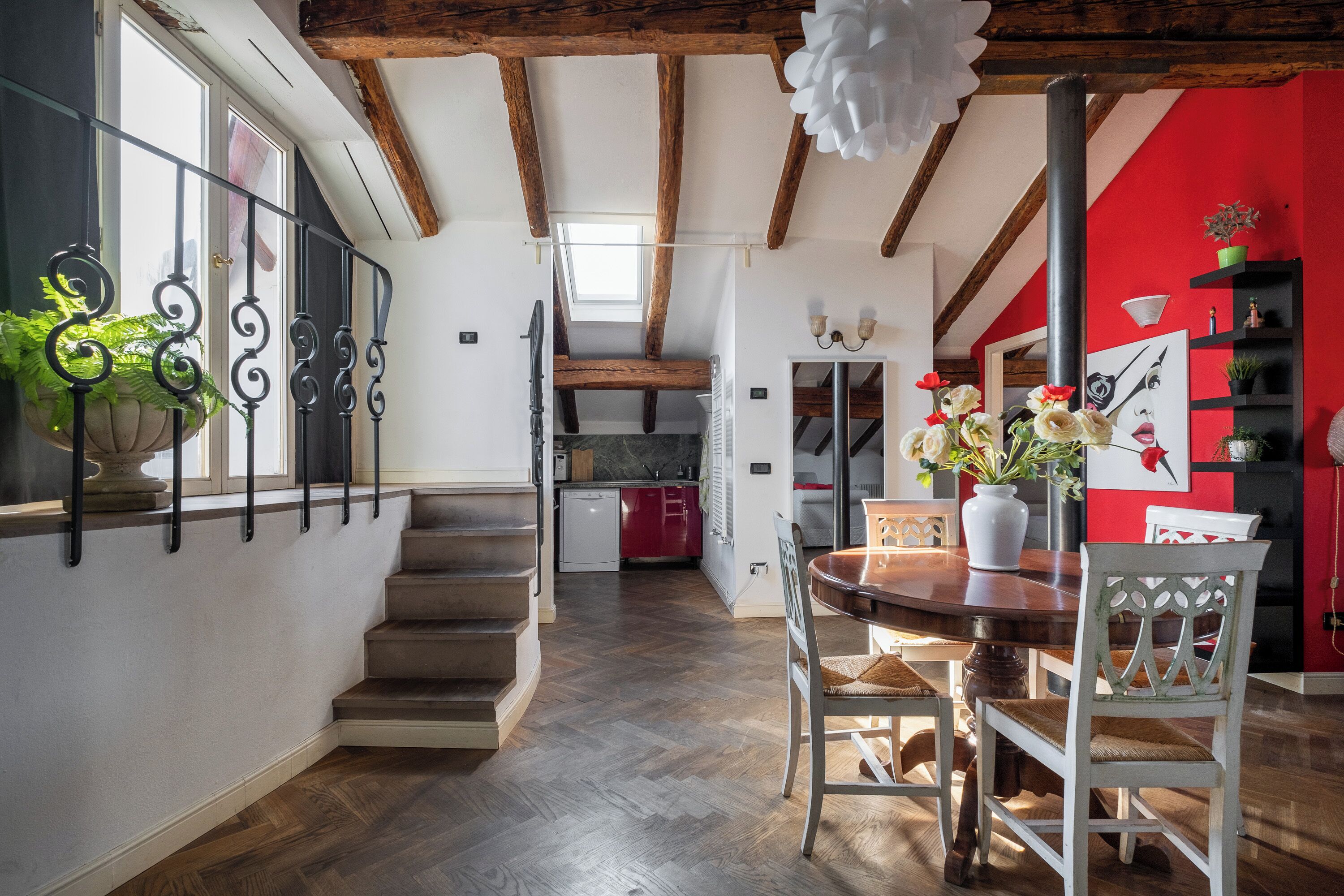 A modern kitchen with wooden beams, a dining area with a round table, and a staircase leading to a second floor.