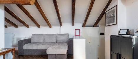 Una sala de estar moderna con un sofá gris, vigas de madera, un armario blanco y un radiador.