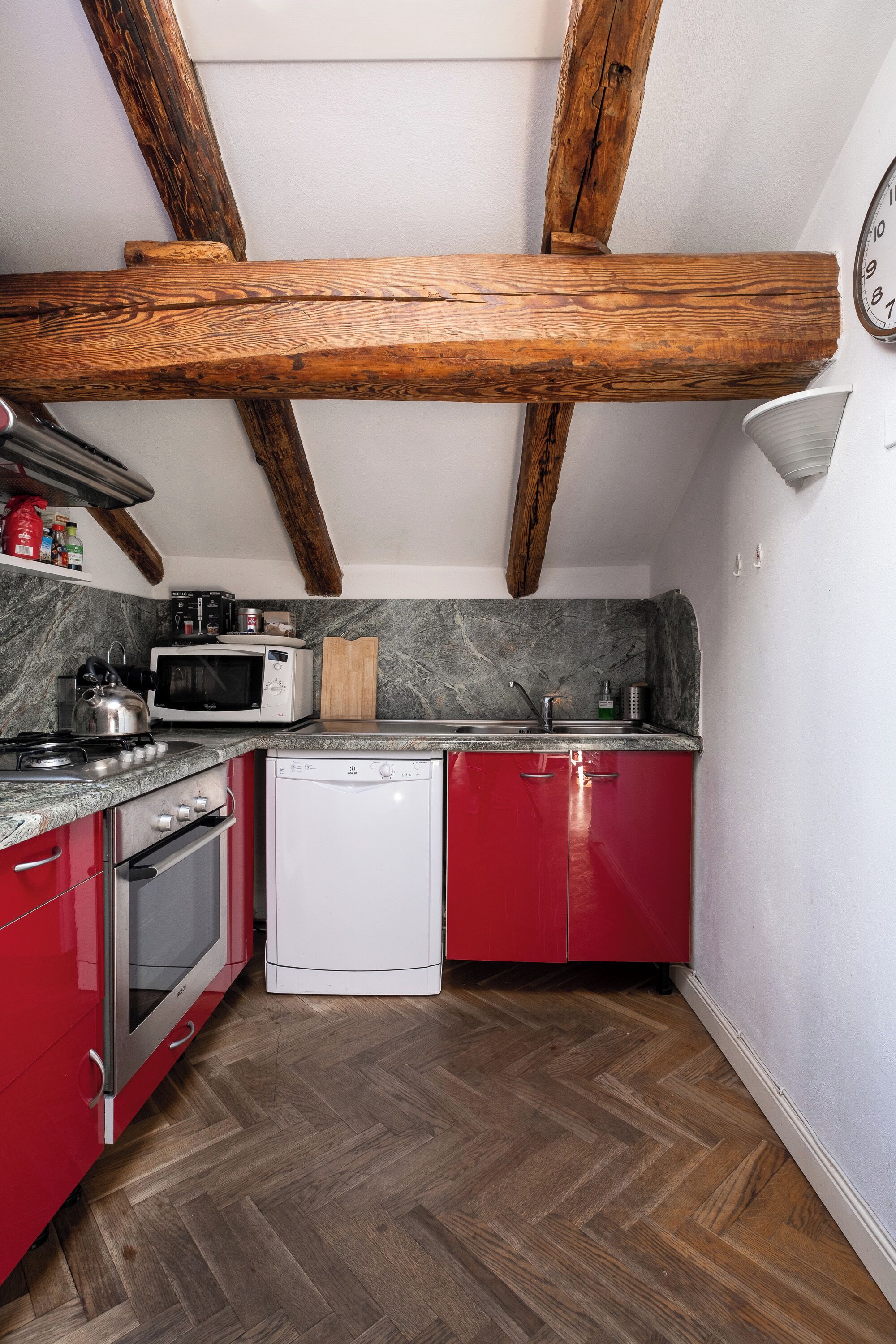 A kitchen with wooden beams, a microwave, a kettle, and red cabinets.