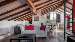 Spazioso loft con travi a vista in legno, un divano grigio con cuscini rossi, un tavolino da caffè nero e vista sulla cucina e zona pranzo.