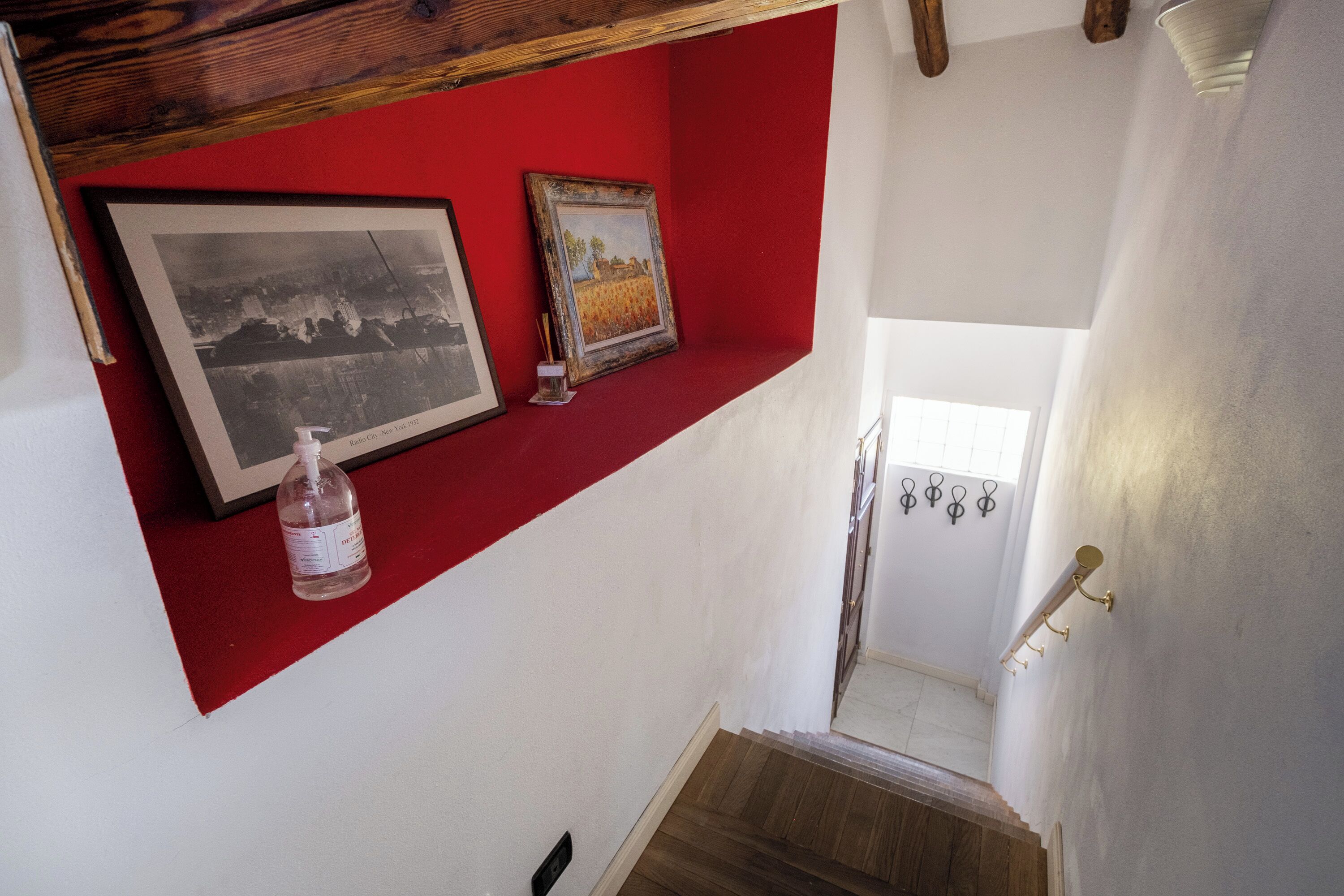 Una escalera con un estante rojo que sostiene cuadros enmarcados y una botella.