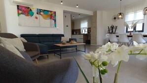 Una sala de estar moderna con sofá, mesa de centro y un comedor con sillas. Se observa una cocina al fondo.
