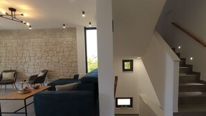 Una sala de estar moderna con pared de piedra, un sofá azul oscuro, una mesa de centro de madera y una escalera de diseño minimalista.
