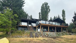Una casa moderna de dos pisos con base de piedra, ventanas grandes y una terraza de madera.
