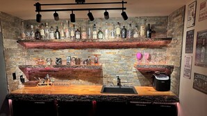 Una zona de bar con estantes llenos de botellas de licor, un lavamanos y una cafetera.