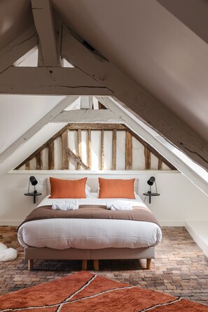 A bedroom with a sloped ceiling, a bed with white and orange bedding, two bedside lamps, and a brick-patterned floor. - Le Perchoir - Appt Rennes parking privé (Rennes)