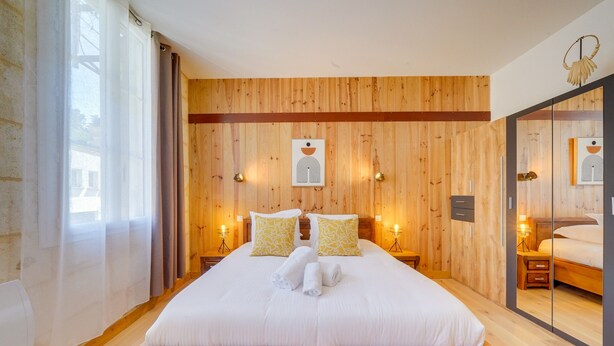 A large bed with white linens and two pillows, wooden paneling on the walls, and two bedside lamps.