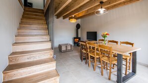 Uma escadaria de madeira leva a uma sala de jantar com uma mesa, cadeiras, uma televisão e uma lareira a lenha.