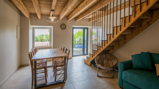 Uma sala de jantar com mesa e cadeiras de madeira, uma escada com corrimão de madeira e um sofá verde.