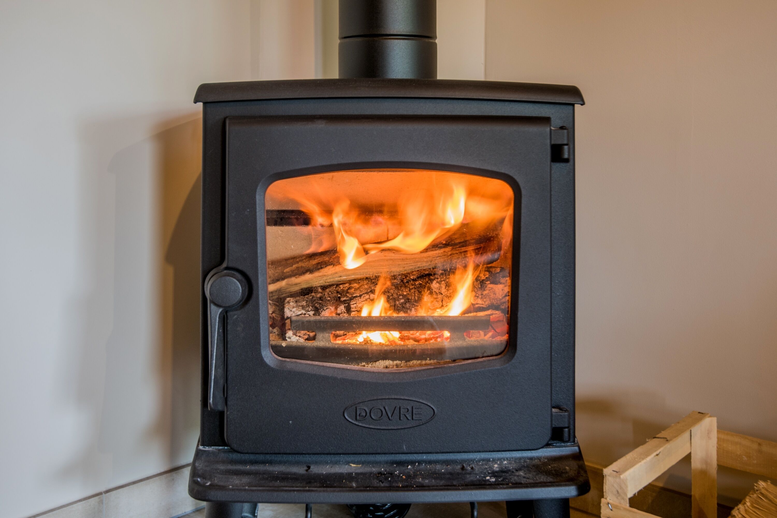 A black wood-burning stove with visible flames, labeled "DOVRE," installed in a corner.