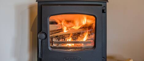A black wood-burning stove with visible flames, labeled "DOVRE," installed in a corner.
