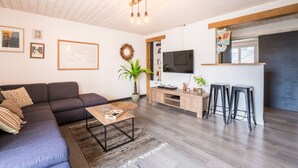 Una sala de estar moderna con un sofá modular, una mesa de centro, un televisor y una zona de bar con taburetes.