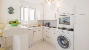 Una cucina moderna con mobili bianchi, forno integrato, lavatrice e una finestra.