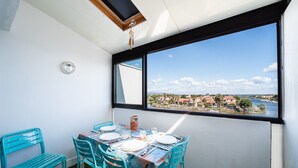Un coin repas avec une table dressée pour quatre personnes, une vue sur une ville côtière et une lucarne au-dessus.