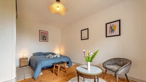 Un dormitorio con cama, mesitas de noche, una silla, una mesa redonda y decoración en la pared.