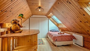 Un dormitorio acogedor en el ático con paredes de madera y techo inclinado, que incluye una cama, un escritorio pequeño y un oso de peluche.