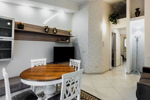 A modern dining area with a wooden table and white chairs, a TV, and decorative items on shelves. - Il giardino di Aci by Wonderful Italy (Catania)