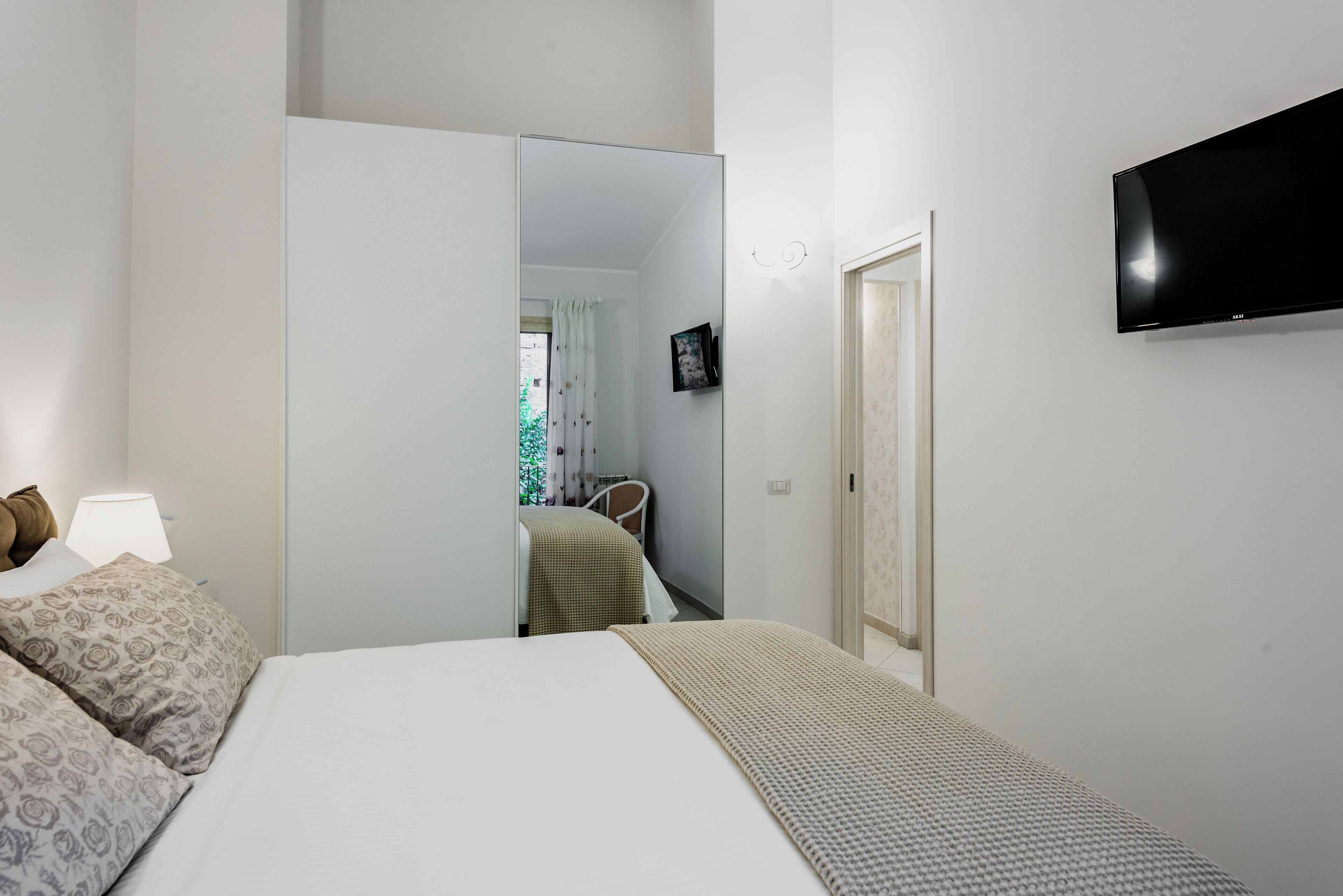 Een hotelkamer met een bed, een televisie, een spiegel en een deur.
