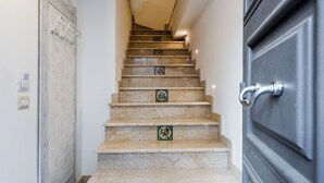 A marble staircase with decorative tiles, a door with a silver handle, and a light switch on the wall.