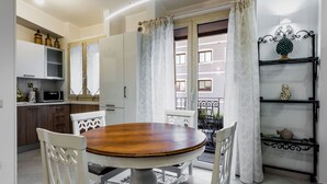 A dining area with a round wooden table, white chairs, and a black and white patterned rug.