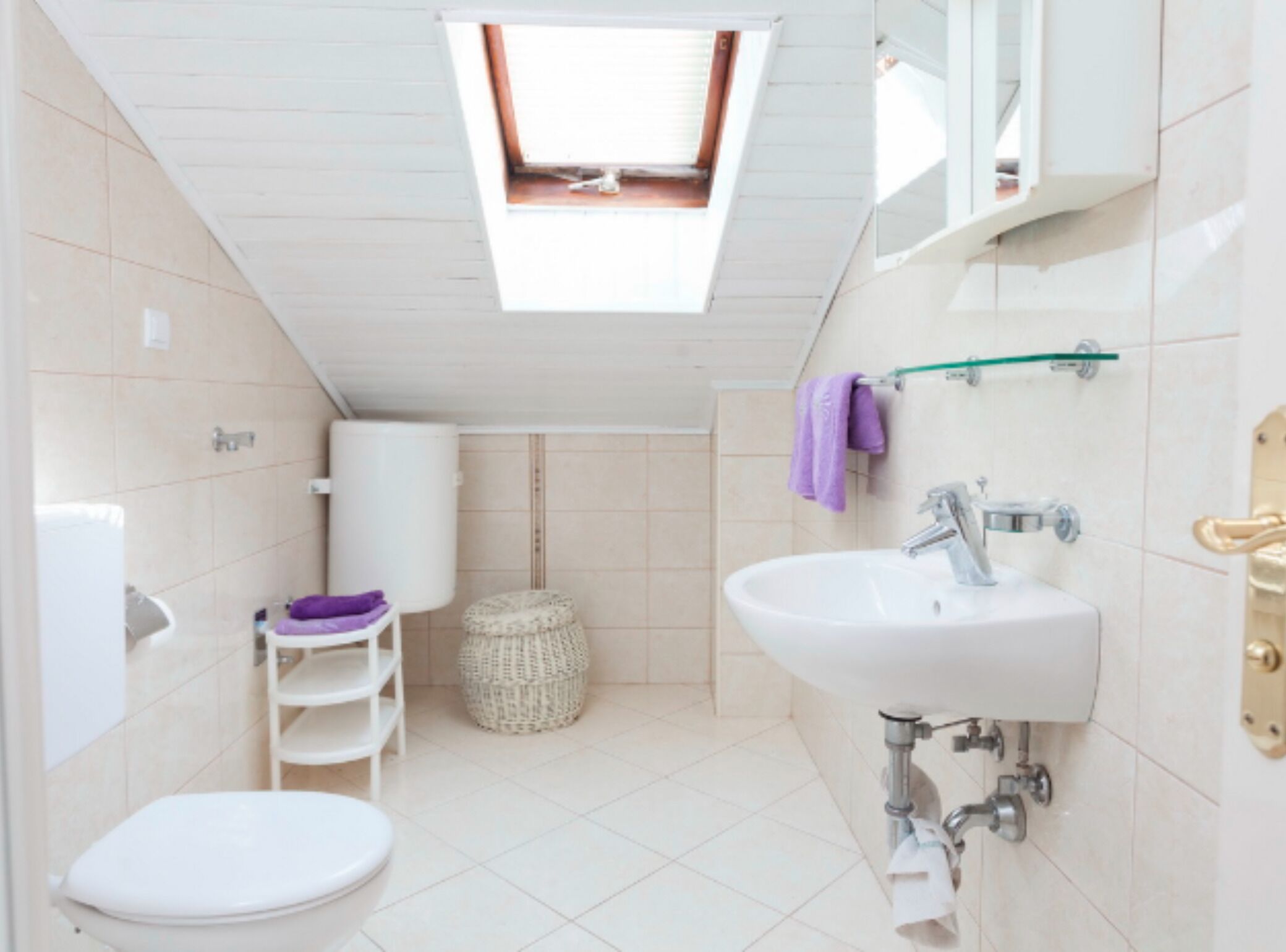 Ein kleines Badezimmer mit Oberlicht, Toilette, Waschbecken und einem kleinen Ablagefach.
