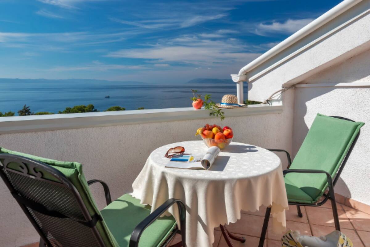 A balcony with a table, chairs, and a view of the sea.