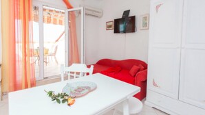 A room with a red sofa, white table, and a TV on the wall. - Apartments Lili (Podgora)