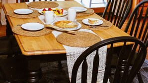 Une table de salle à manger en bois, avec des assiettes, des couverts et un panier de fruits.